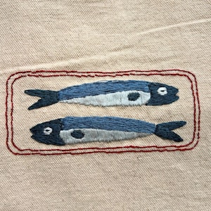 Finished product: 2 embroidered sardines facing opposite directions inside of a red tin can.