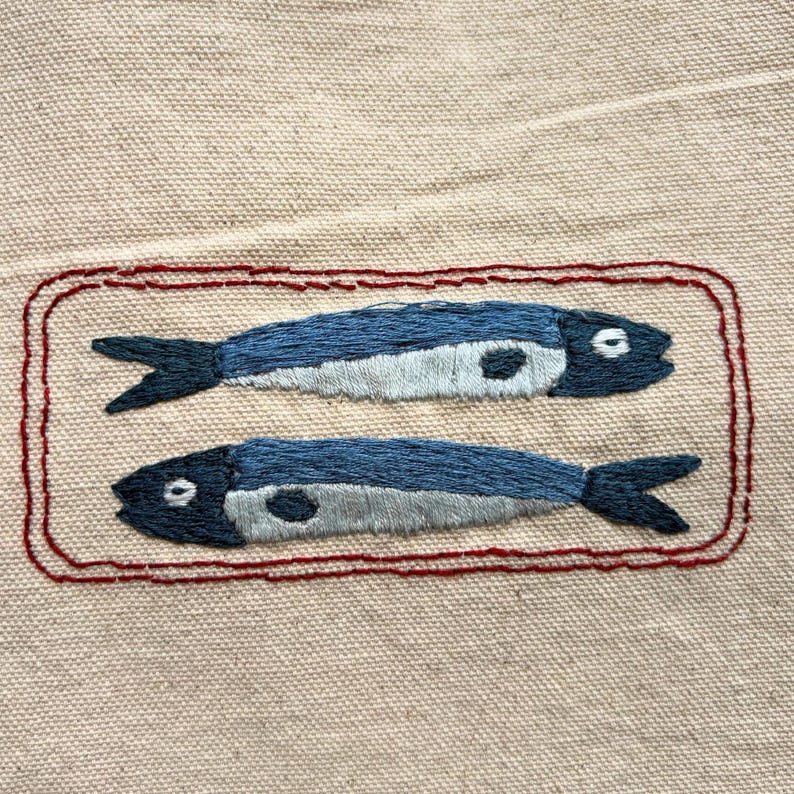 Finished product: 2 embroidered sardines facing opposite directions inside of a red tin can.
