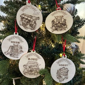 May include: Five wooden Christmas ornaments with different engine designs. Each ornament features a different engine type, including a 2JZ, VR38, RB26, EJ20, and 4G63T. The ornaments are all round and have a white background with black outlines.