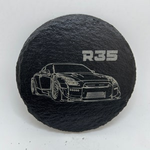 May include: A black slate coaster with a white outline of a Nissan Skyline R35 car and the text "R35" in white.