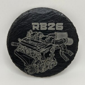 May include: A black slate coaster with a silver engraved image of an RB26 engine. The text "RB26" is also engraved on the coaster.