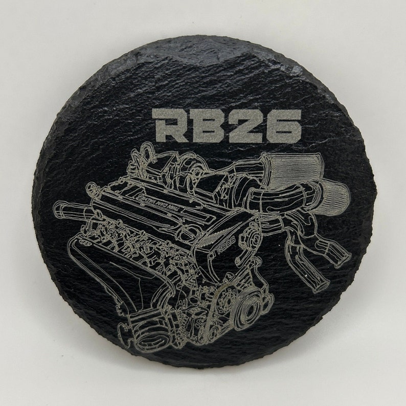May include: A black slate coaster with a silver engraved image of an RB26 engine. The text "RB26" is also engraved on the coaster.