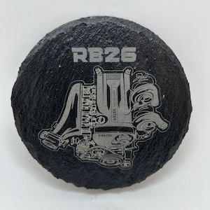 May include: Black slate coaster with a silver engraving of a Nissan RB26 engine. The engine is depicted in detail, with the text "RB26" and "NISSAN" visible.