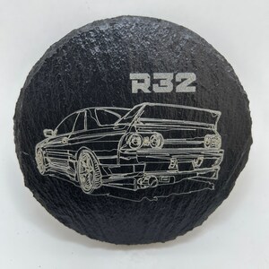 May include: A black slate coaster with a silver outline of a Nissan Skyline R32 car and the text "R32" on the top.
