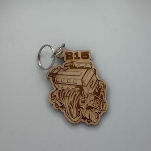 May include: A light-colored wooden keychain featuring a laser-engraved illustration of a car engine with the text B16 positioned at the top. The keychain includes a circular silver metal split ring attached to the top for securing keys.