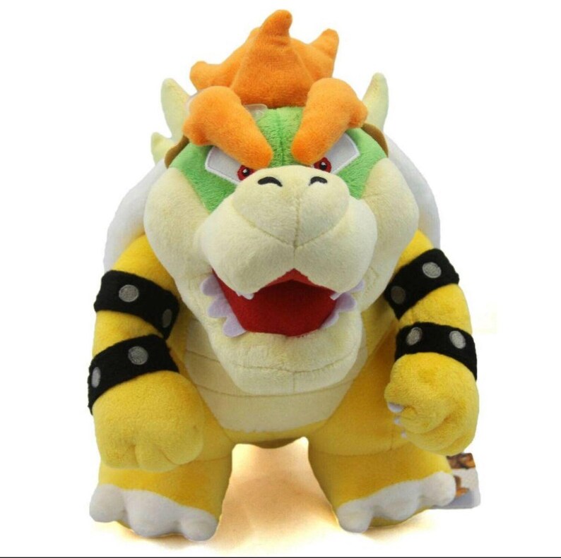 Pu&ograve; includere: Un peluche giallo e verde di Bowser, un personaggio della serie di videogiochi Super Mario. Bowser ha una corona arancione a punta e un'espressione feroce.