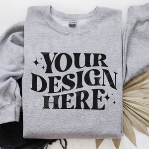 May include: A grey sweatshirt with the text "YOUR DESIGN HERE" in black lettering. The sweatshirt has a crew neck and long sleeves.