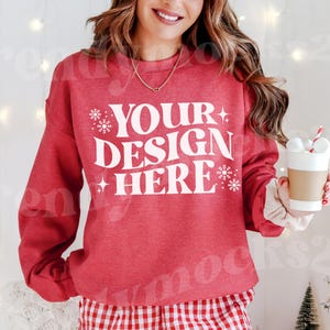 May include: Red sweatshirt with white text that says 'Your Design Here' with snowflakes on either side of the text. The sweatshirt has a distressed look.