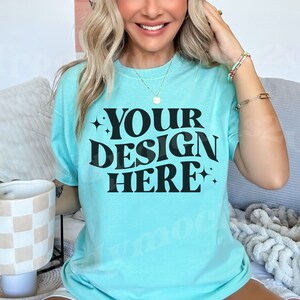 May include: A light blue t-shirt with the text "YOUR DESIGN HERE" in black. The shirt is a solid color and has a relaxed fit. The image also shows a decorative candle holder and jewelry.