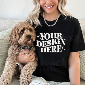 May include: A black t-shirt with the text 'YOUR DESIGN HERE' in white retro-style font. The t-shirt is being worn by a person and a brown dog is sitting on their lap.