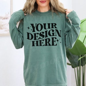 May include: A teal long-sleeved shirt with the text "YOUR DESIGN HERE" in black.