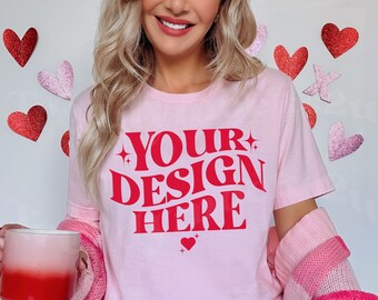 Puede incluir: Camiseta rosa claro con el texto rojo "YOUR DESIGN HERE". La persona sostiene una taza degradada roja y blanca. El fondo tiene decoraciones de corazones rojos y rosas.