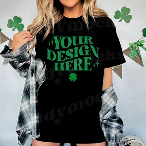Puede incluir: Una camiseta negra con un trébol verde y el texto "YOUR DESIGN HERE" en una fuente retro.