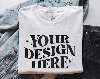 May include: A white t-shirt with the text "YOUR DESIGN HERE" in black retro-style lettering with small stars on either side.