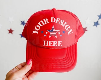Może przedstawiać: Czerwona czapka trucker z siatką z tyłu. Z przodu czapki znajduje się biała gwiazda z czerwonymi i niebieskimi paskami oraz napis "YOUR DESIGN HERE" w kolorze białym.