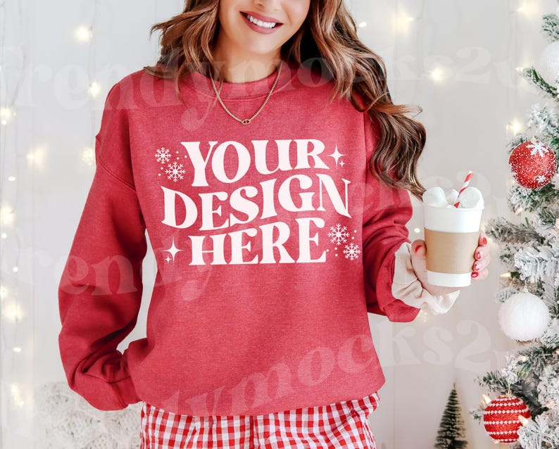 May include: Red sweatshirt with white text that says 'Your Design Here' with snowflakes on either side of the text. The sweatshirt has a distressed look.