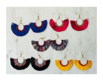 May include: Assortment of colorful tassel earrings with gold hoops. The earrings are made with a variety of colors, including red, blue, yellow, black, and white.