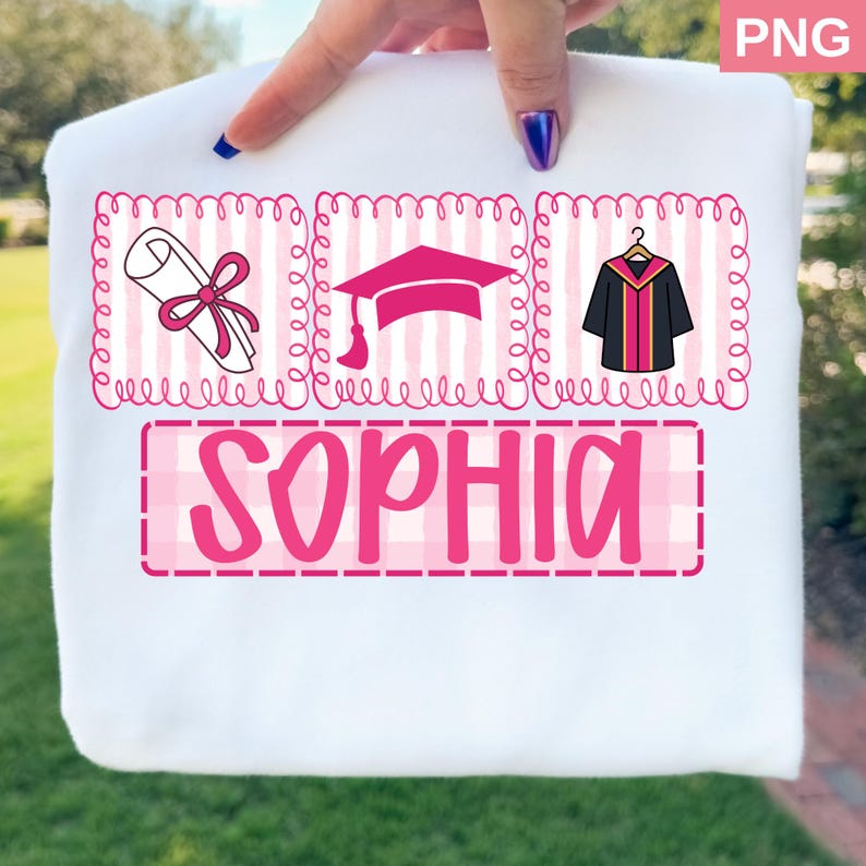 May include: White t-shirt with a pink graduation-themed design. The design includes a diploma, graduation cap, and gown, along with the name "SOPHIA" in a pink plaid font. The graphics are framed with pink curly borders.