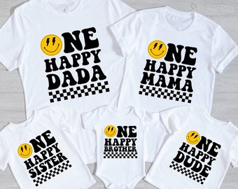 May include: Set of five white t-shirts with black and yellow graphic designs. The shirts feature a smiley face with lightning bolts and the text "One Happy" followed by "Dada", "Mama", "Sister", "Brother", and "Dude".