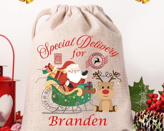 May include: A beige burlap Christmas gift bag with a drawstring closure. The bag features a festive design with Santa Claus in a sleigh, a reindeer, and the text "Special Delivery for Branden". The top of the bag says "Customize name".