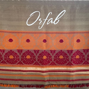 Puede incluir: Un chal tejido marrón con rayas naranjas y burdeos y una inscripción blanca que dice "Orfab".