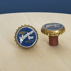 Puede incluir: Dos tapones de botella dorados con etiquetas azules y blancas que dicen "Wieselburger Bier" y "Seit 1776".