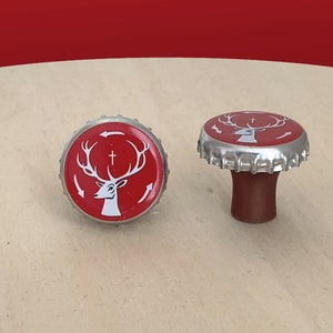 May include: Two red bottle caps with a silver rim and a white deer with antlers and a cross on its head. The deer is surrounded by white arrows.