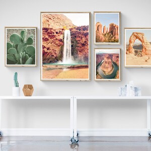 Puede incluir: Una colecci&oacute;n de impresiones enmarcadas de paisajes des&eacute;rticos, que incluyen una cascada, un cactus y un arco natural. Las impresiones se exhiben en una mesa rodante blanca, creando una est&eacute;tica de pared de galer&iacute;a.