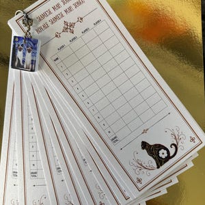 May include: A stack of white score sheets for Siamese Mah Jongg with brown printed borders, text, and a grid for four players. A small square charm featuring two Siamese cats is attached to the top left corner with a metal ball chain.