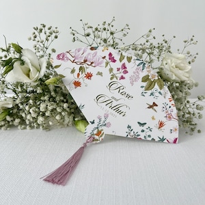 May include: A white wedding fan with a floral design and the text "Rose and Arthur 12.12.2025". The fan has a pink tassel.