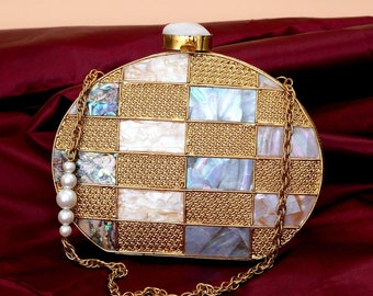 May include: A round, gold-tone clutch bag with a checkered pattern of white and iridescent mother-of-pearl shell pieces. The bag has a gold chain strap and a white pearl detail.