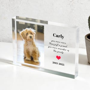 Puede incluir: Un bloque acrílico transparente con una foto de un perro pequeño de color marrón claro. El bloque tiene el texto "Carly, eras más que un amigo, eras un miembro de la familia" con un corazón rojo y las fechas 2013-2025.