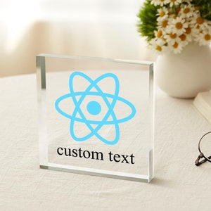 Puede incluir: Un pisapapeles de vidrio transparente con un símbolo de átomo azul y el texto "custom text" impreso en la parte inferior.