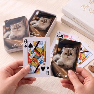 May include: A deck of custom playing cards featuring a photograph of a fluffy light-colored cat on the back of each card with the text Mito and a paw print icon. The set includes a white metal storage tin with the same cat image on the lid.