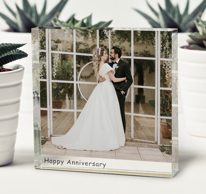 May include: A glass photo block with a wedding photo of a couple in a white dress and a black suit. The photo is set against a white lattice background. The text "Happy Anniversary" is printed on the bottom of the block.