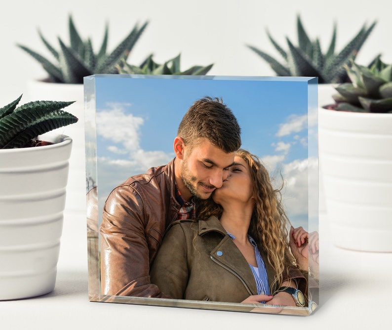 May include: A couple in brown leather jackets, the woman is kissing the man on the cheek, against a blue sky with white clouds.
