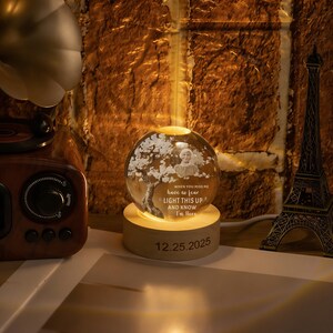 May include: A glowing glass sphere with a tree and a person's image, set on a wooden base. The sphere has the text "WHEN YOU MISS ME have no fear LIGHT THIS UP AND KNOW I'm Here" and the date "12.25.2025".