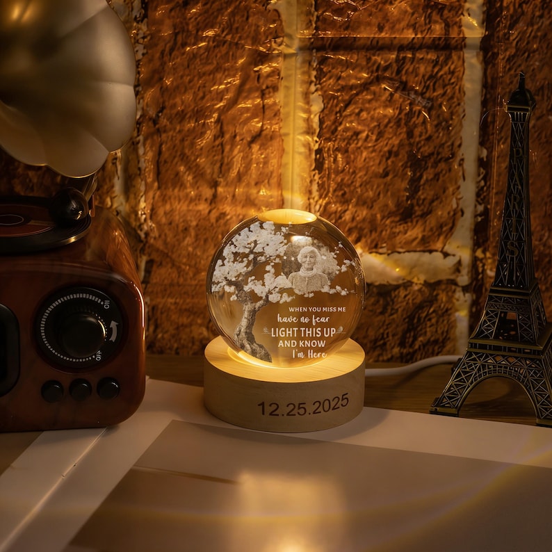 May include: A glowing glass sphere with a tree and a person's image, set on a wooden base. The sphere has the text "WHEN YOU MISS ME have no fear LIGHT THIS UP AND KNOW I'm Here" and the date "12.25.2025".