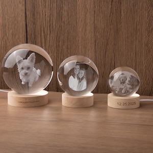 May include: Three illuminated glass spheres with engraved images of a dog, a mother and daughter, and a dog with a person. Each sphere sits on a wooden base. The largest sphere has the text "Love is a her biggest word".