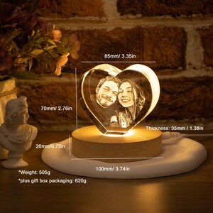 May include: A heart-shaped crystal photo featuring a couple, lit by a warm glow. The crystal is 8.5cm wide, 7cm high, and 3.5cm thick, set on a wooden base. The base sits on a white circular platform. The weight is 505g.