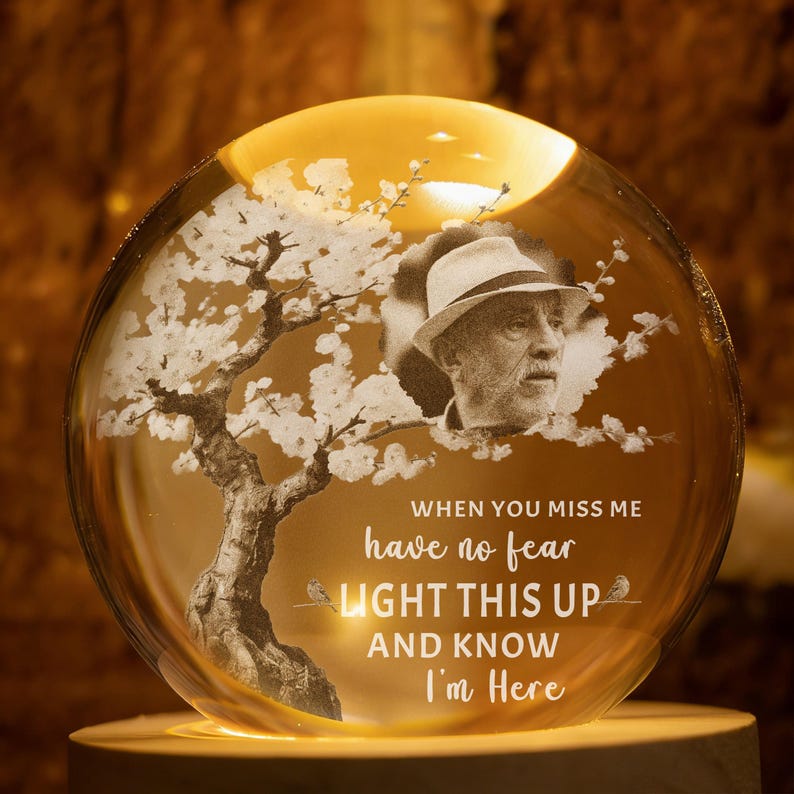 May include: A glowing, spherical memorial lamp with a portrait and a tree design. The lamp features the text "When you miss me, have no fear, light this up and know I'm here." The lamp is lit from within, creating a warm, inviting glow.