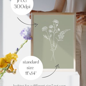 Puede incluir: Una descarga digital imprimible de una ilustraci&oacute;n de l&iacute;nea de un ramo de flores sobre un fondo verde salvia. El texto "Recuerda siempre que eres amado" est&aacute; escrito en cursiva en los tallos de las flores. La imagen est&aacute; enmarcada y la sostiene una persona. El texto "tama&ntilde;o est&aacute;ndar 11"x14" est&aacute; debajo de la imagen.