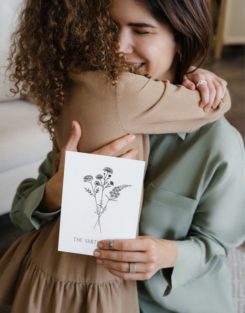 Puede incluir: Una mujer y una ni&ntilde;a se abrazan mientras sostienen una tarjeta con un dibujo en blanco y negro de flores y el texto "THE SMITHS".