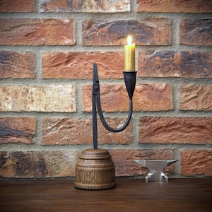 May include: A candle holder with a lit candle, featuring a black metal arm and a wooden base. The candle holder is set against a brick wall. A small metal anvil is also visible.