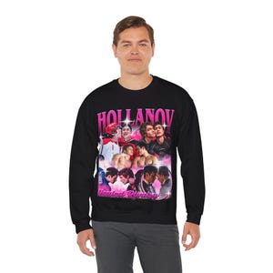 May include: Black crewneck sweatshirt featuring a graphic design with the text "HOLLANOV" in pink letters. The design includes images of several young men. Below the text is the phrase "Heated Rivalry" in pink.
