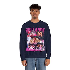 May include: Navy blue sweatshirt featuring a collage of images with the text "HOLLANOV" in pink, and "Heated Rivalry" in pink below the collage. The sweatshirt is a crew neck style.