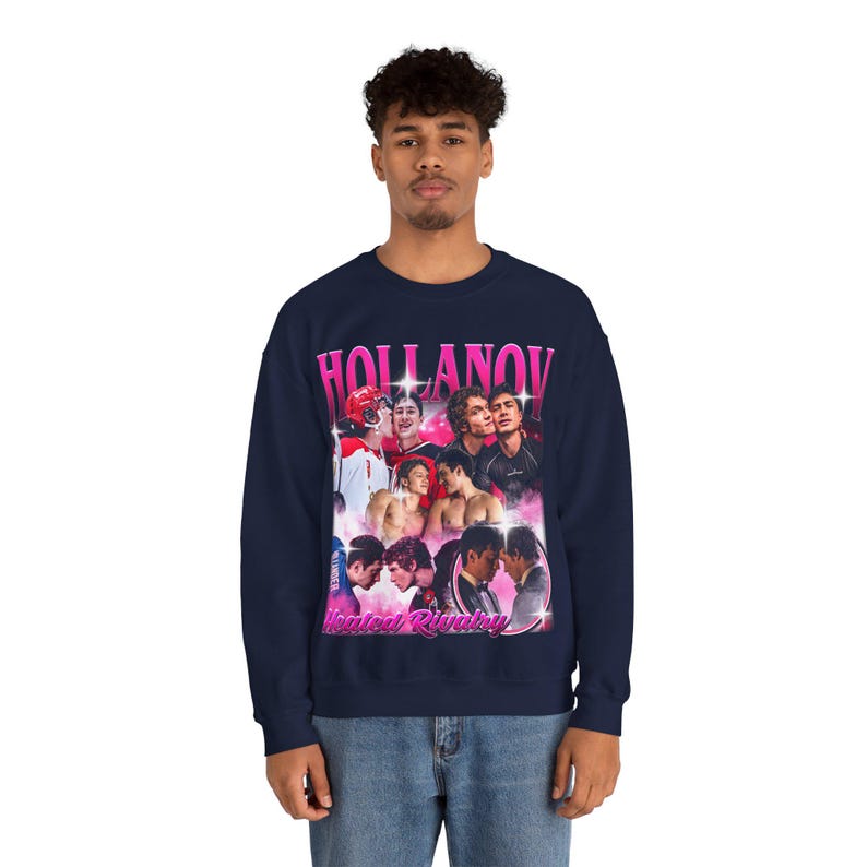 May include: Navy blue sweatshirt featuring a collage of images with the text "HOLLANOV" in pink, and "Heated Rivalry" in pink below the collage. The sweatshirt is a crew neck style.