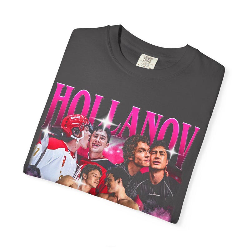 May include: Dark gray t-shirt featuring a graphic with the word "HOLLANOV" in pink, with a photo of several young men. One man is wearing a hockey helmet and jersey. The shirt has a crew neck and short sleeves.