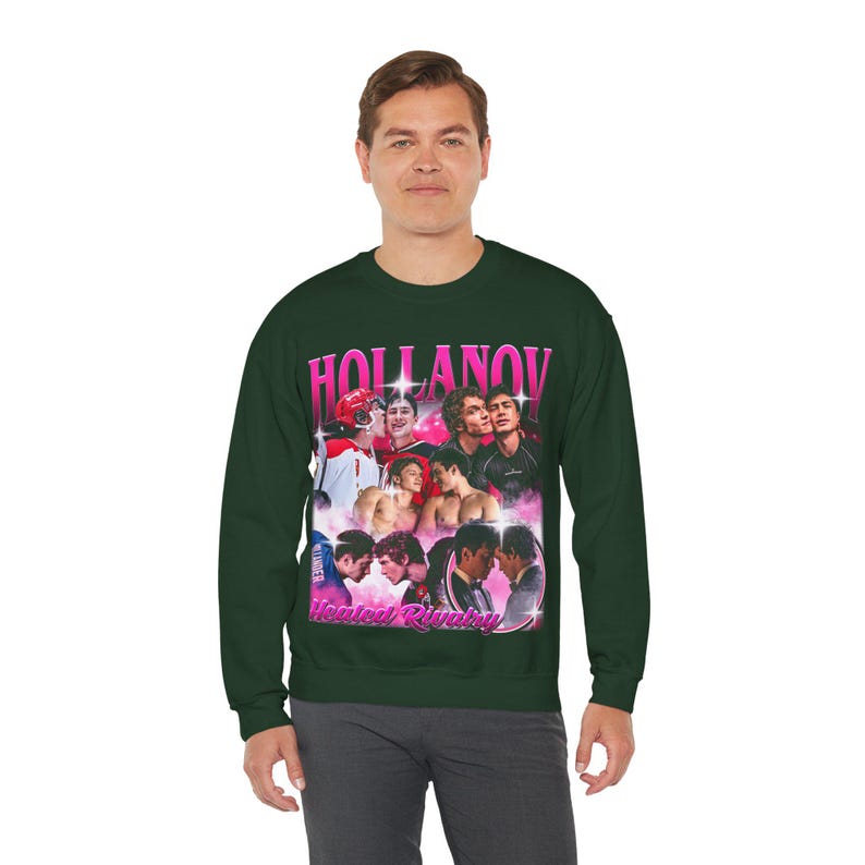 May include: Dark green sweatshirt featuring a graphic design with the word "HOLLANOV" in pink, along with images of people. Below the main text is the phrase "Heated Rivalry" in pink. The sweatshirt is a crew neck style.