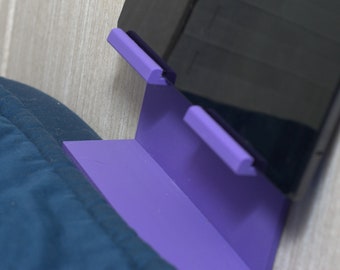May include: A purple tablet stand with two slots for holding devices. The stand is mounted on a wall and has a sleek, modern design.